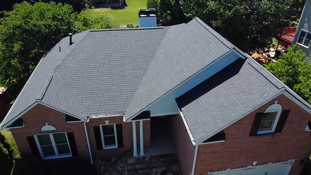Aerial view of a residential brick home with a newly installed asphalt shingle roof completed through an insurance claim restoration